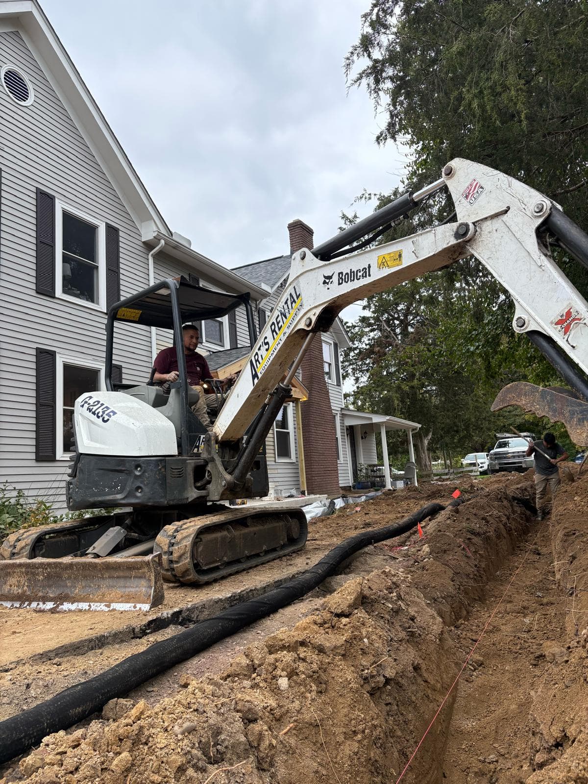 Mini excavator digging a drainage trench alongside a residential home